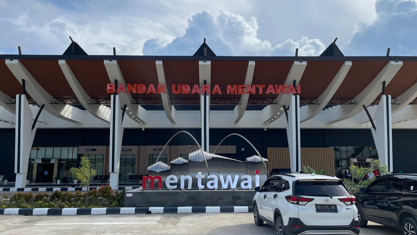 The entrance to Mentawai Islands new airport with large red letters spelling 'Bandar Udara Mentawai' suspended above a water feature with the word mentawai